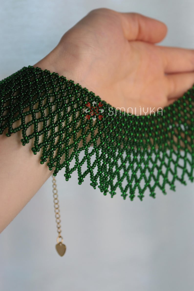 K&ouml;nnte beinhalten: Eine gr&uuml;ne Perlenkette mit einer zarten Kette und einem Herzanh&auml;nger. Die Kette besteht aus kleinen, runden Perlen, die in einem komplizierten Muster miteinander verwoben sind.