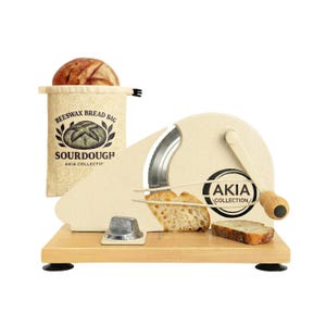May include: A cream-colored manual bread slicer with a wooden base, a circular blade, and a hand crank. The slicer features the text AKIA COLLECTION. Beside it sits a beige beeswax bread bag with a sourdough illustration and text.