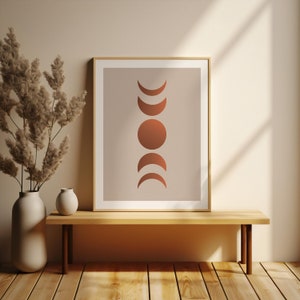 May include: A framed print with a minimalist design featuring a series of copper-colored moons and a circle in a vertical arrangement on a light beige background.