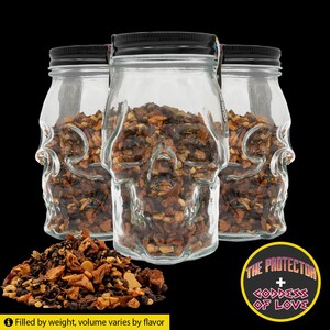 May include: Three clear glass jars shaped like skulls, filled with a mix of dried ingredients. Each jar has a black lid. A pile of the ingredients sits in front of the jars. The text "THE PROTECTOR + GODDESS OF LOVE" is in a yellow circle.