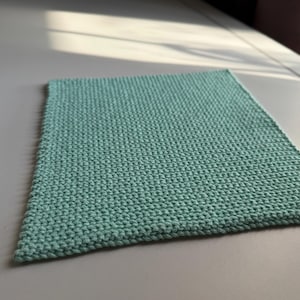 Puede incluir: Un paño de lavado rectangular, tejido a mano, en un suave color verde azulado. El primer plano resalta las puntadas texturizadas y en bucle de la tela. El paño de lavado está hecho de un material suave y es adecuado para su uso en el baño.