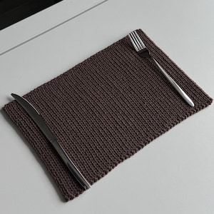 Peut inclure: Un set de table rectangulaire marron foncé avec une texture tissée, accompagné d'une fourchette et d'un couteau en acier inoxydable. L'ensemble est disposé sur une surface blanche. Présentation d'une table simple et élégante.