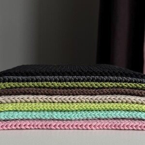 Puede incluir: Una pila de cuadrados de tela de punto coloridos. Los colores incluyen negro, verde oliva, marr&oacute;n, beige, verde claro, aguamarina y rosa. La tela tiene un aspecto texturizado y trenzado.