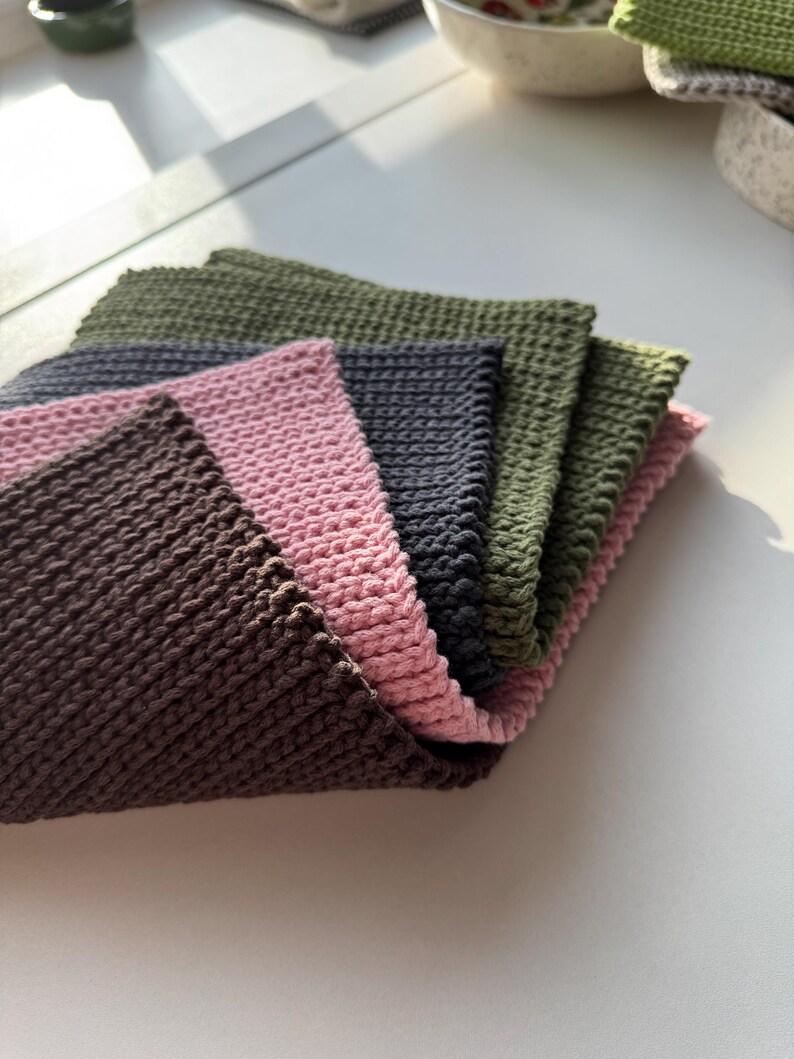 Puede incluir: Una pila de seis pa&ntilde;os cuadrados de tejido de punto en varios colores: marr&oacute;n, rosa, gris y verde oliva. Los pa&ntilde;os est&aacute;n cuidadosamente dispuestos, con los bordes de cada pa&ntilde;o visibles, mostrando el patr&oacute;n de tejido texturizado. Sobre una superficie blanca.