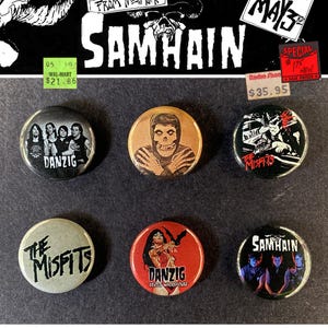 Può includere: Una collezione di sei spille rotonde con loghi e opere d'arte di band. Le spille presentano le band Danzig, The Misfits e Samhain. Le spille hanno vari schemi di colore, tra cui nero, rosso e oro.
