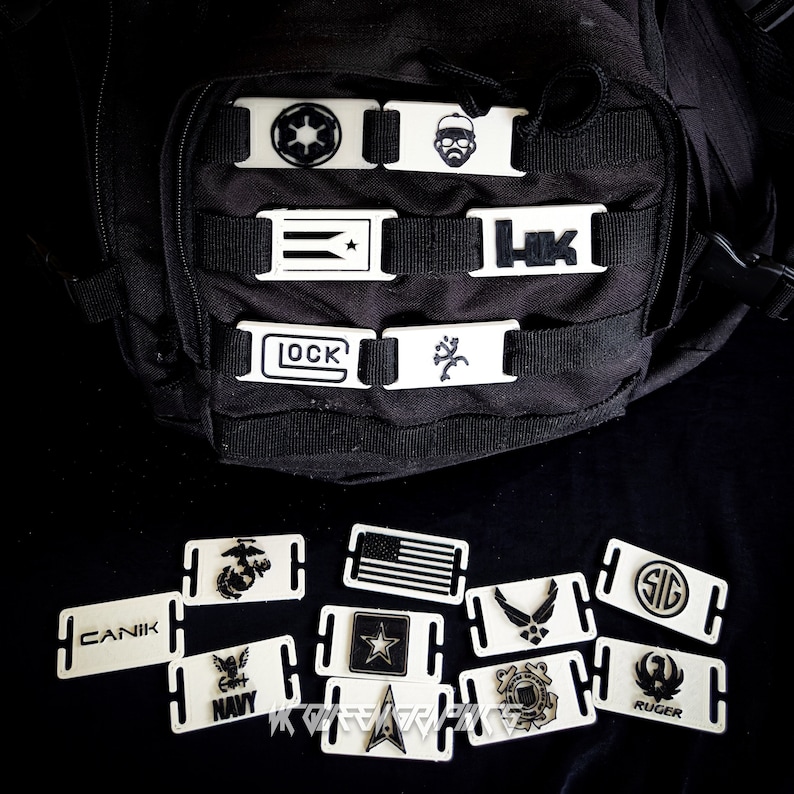 May include: A collection of white plastic buckle straps with various logos and designs, including a star wars logo, a US flag, a military logo, and a Ruger logo. The straps are arranged on a black surface.