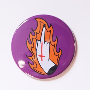 Puede incluir: Un botón morado con una mano blanca haciendo el dedo medio, rodeado de llamas naranjas.