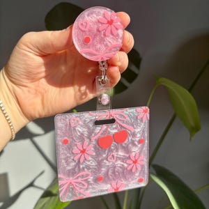 Marqueur Parker à motif floral, cerises et noeud, avec enrouleur assorti et fond rose irisé.