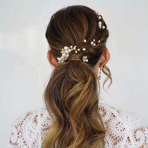 May include: A low ponytail hairstyle with loose waves and a pearl and gold hair accessory.