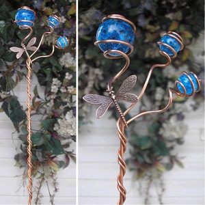 May include: A copper wire garden stake with a dragonfly design and three blue glass orbs. The stake is twisted and has a rustic look.