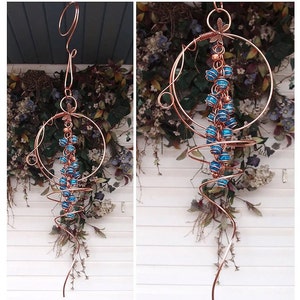 May include: Copper-colored wind chime with a spiral design and a circular frame. The chime features blue glass beads and a dragonfly accent. The decorative piece is suspended from a hook, suitable for outdoor or indoor decor.