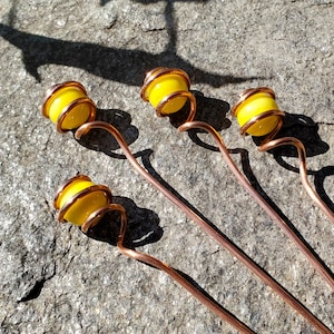 May include: Four copper wire swirls with yellow glass beads at the end of each swirl. The swirls are on a gray textured surface.
