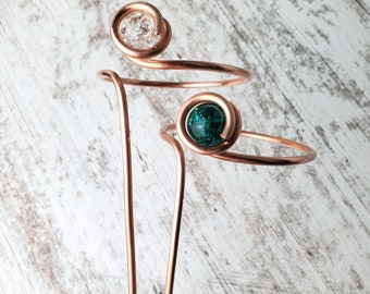 May include: Two copper wire bracelets with a green and a clear glass bead. The bracelets are wrapped around each other.