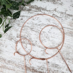 May include: Three copper wire hoops of different sizes, the largest hoop is on the bottom and the smallest hoop is on top. The hoops are on a white wooden surface.