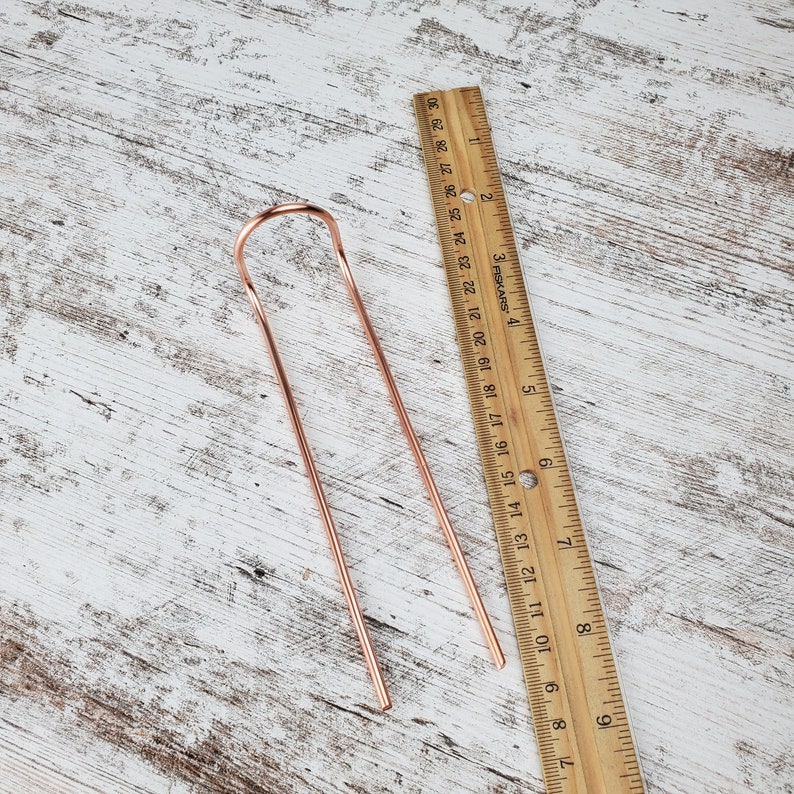 May include: A pair of rose gold hair sticks with a simple loop design. The sticks are about 7 inches long and are shown next to a ruler.