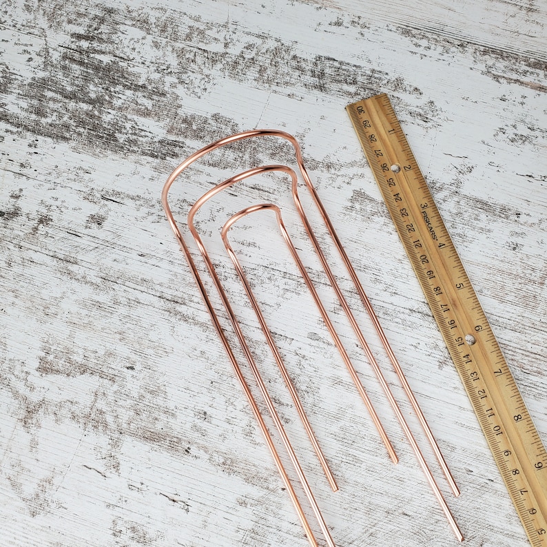 May include: Set of three copper wire hoops, nested together, on a white wooden surface. The hoops are different sizes and are all open at the top.