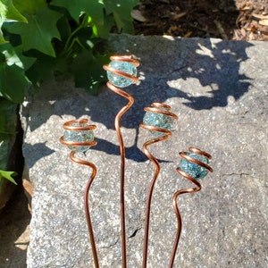 May include: Four copper wire garden stakes with a spiral design topped with blue glass marbles.