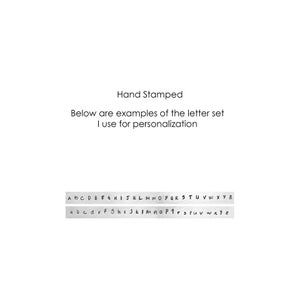 May include: A close-up of a sample alphabet set for hand stamping. The letters are shown in both uppercase and lowercase. The text reads "Hand Stamped Below are examples of the letter set I use for personalization."