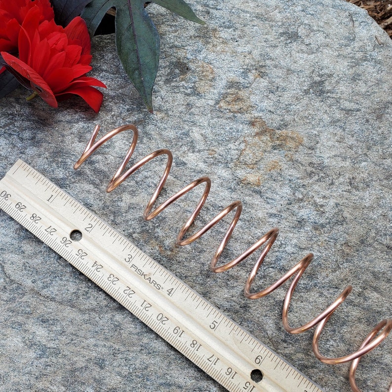 May include: A copper-colored metal spring coil on a gray textured surface with a ruler marked in inches and the text "3 FISKARS 4".