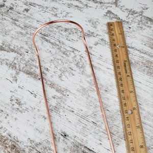 May include: A copper-colored metal hanger with a rounded top and two straight legs. The hanger is approximately 8 inches long.