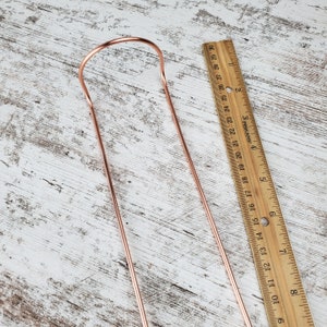 May include: A copper-colored metal straw with a bent end, measured against a wooden ruler. The straw is approximately 8 inches long.