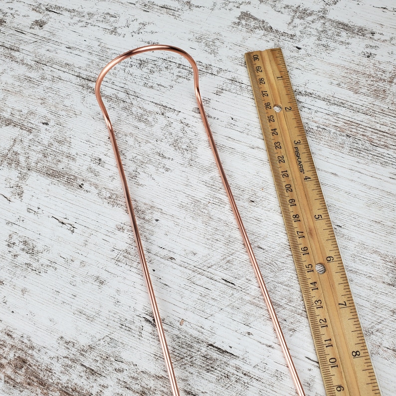 May include: A copper-colored metal straw with a bent end, measured against a wooden ruler. The straw is approximately 8 inches long.