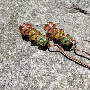 May include: Two copper wire hair pins with green, yellow, and pink glass beads. The beads are wrapped in copper wire and have a sparkly finish.
