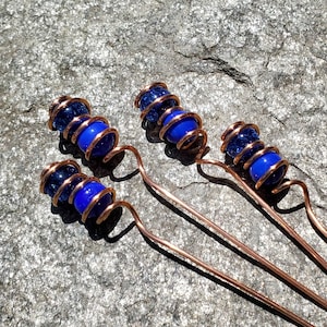 May include: Four copper wire garden stakes with blue glass beads. The beads are wrapped in copper wire and have a sparkly finish.