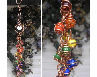 May include: A copper wire wind chime with a rainbow of colored glass beads. The beads are wrapped in copper wire and hang from a copper wire loop. The wind chime is decorated with a small copper tag with the word "Wish" written on it.