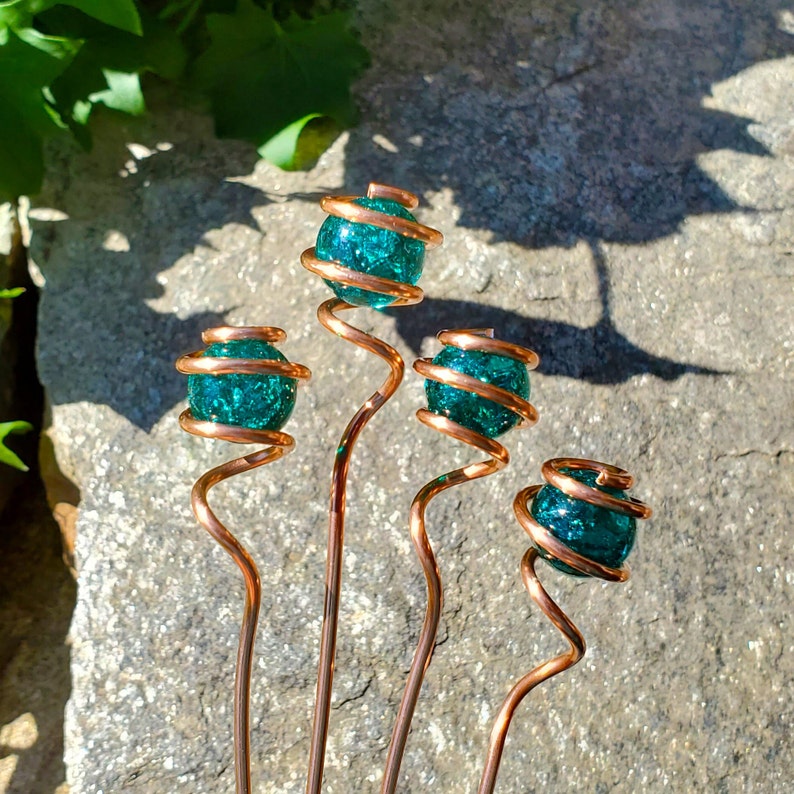 May include: Five copper wire garden stakes with teal blue glass orbs at the top. The orbs have a sparkly, textured finish.