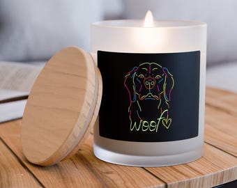 Op de afbeelding: Een matglazen kaarsglas met een zwart label met een kleurrijke lijnillustratie van een hondenkop en het woord "woof" met een hartje. Het kaarsglas heeft een houten deksel.
