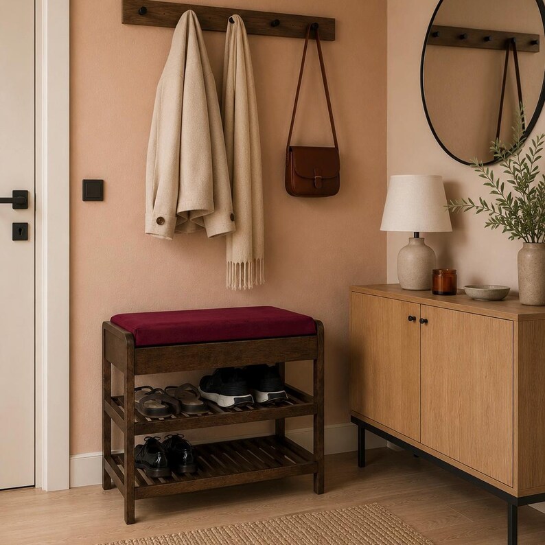 May include: A dark wood shoe rack with a deep red cushioned seat on top and two slatted shelves below. The rack holds several pairs of shoes, including black sneakers and dress shoes, providing a functional storage solution for an entryway.