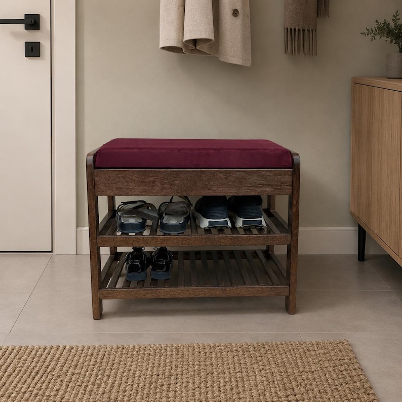 May include: A dark brown wooden shoe bench featuring a deep burgundy upholstered seat cushion. The bench includes two slatted storage shelves underneath, currently holding several pairs of casual footwear, including sneakers and sandals.