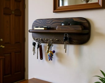 May include: A dark stained wooden key holder with a shelf and brass hooks. The shelf holds a pen and sunglasses. Several sets of keys hang from the hooks, including a key with a cartoon character.