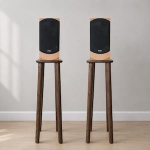 May include: Two light wood speakers with black mesh grilles and the brand name SVEN printed in white, each resting on a tall, dark brown wooden stand with four slender, tapered legs that provide a stable base for the audio equipment.