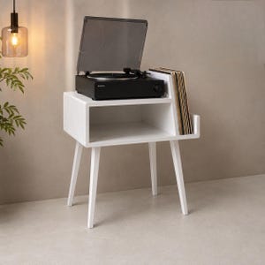 May include: A white wooden record player stand with four tapered legs, featuring an open storage shelf and a vertical slot for vinyl records. A black Sony turntable with a transparent dust cover is positioned on the top surface of the stand.