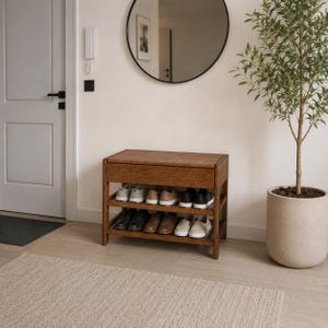 Può includere: Una panca rettangolare in legno per riporre le scarpe con una superficie superiore piatta e due ripiani aperti. L'unità presenta una finitura in venature del legno marrone medio e contiene diverse paia di scarpe casual disposte sui ripiani.