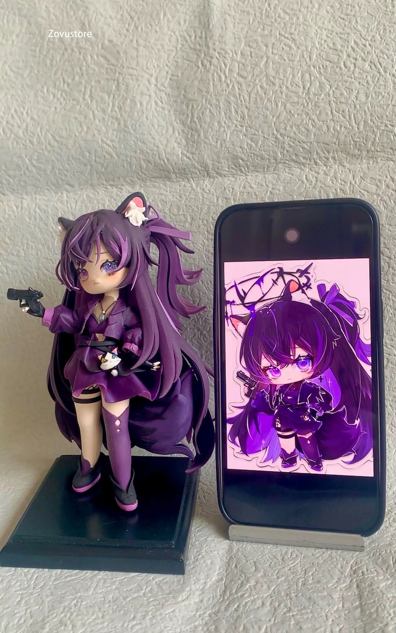 May include: A purple anime character figurine with a gun, cat ears, and a ponytail. The figurine is standing on a black base. The figurine is next to a smartphone with a similar image on the screen.
