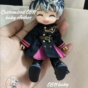 Op de afbeelding: Een zwarte en roze outfit met gouden accenten voor een pop. De pop heeft zwart haar en draagt zwarte schoenen. De tekst "Customized OB11 baby clothes" is zichtbaar in de afbeelding.
