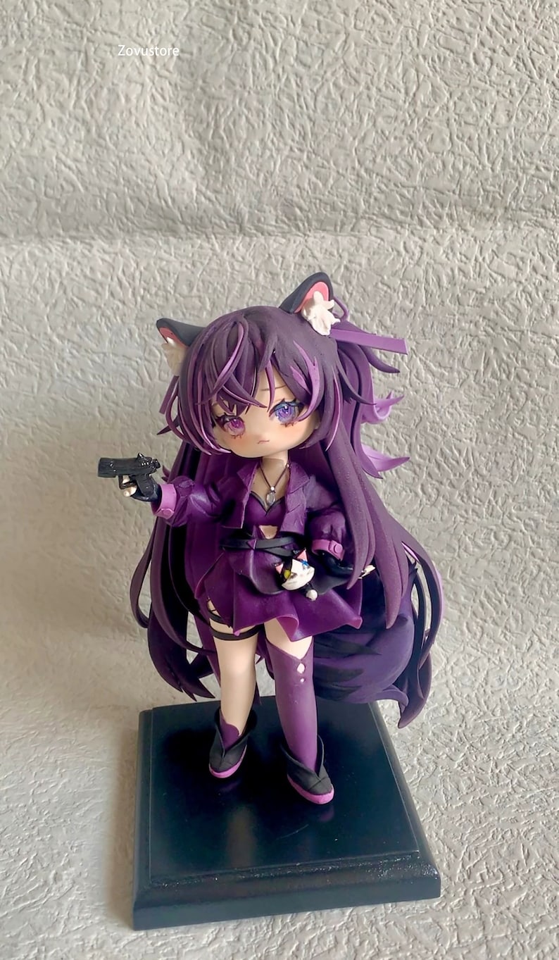 May include: Purple anime figurine with cat ears, holding a black gun, wearing a purple dress and boots, standing on a black base.