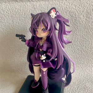 May include: Purple anime figurine with long hair, wearing a purple dress, holding a black gun and a small white cat. The figurine is standing on a black base.