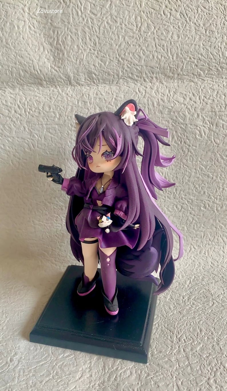 May include: Purple anime figurine with long hair, wearing a purple dress, holding a black gun and a small white cat. The figurine is standing on a black base.