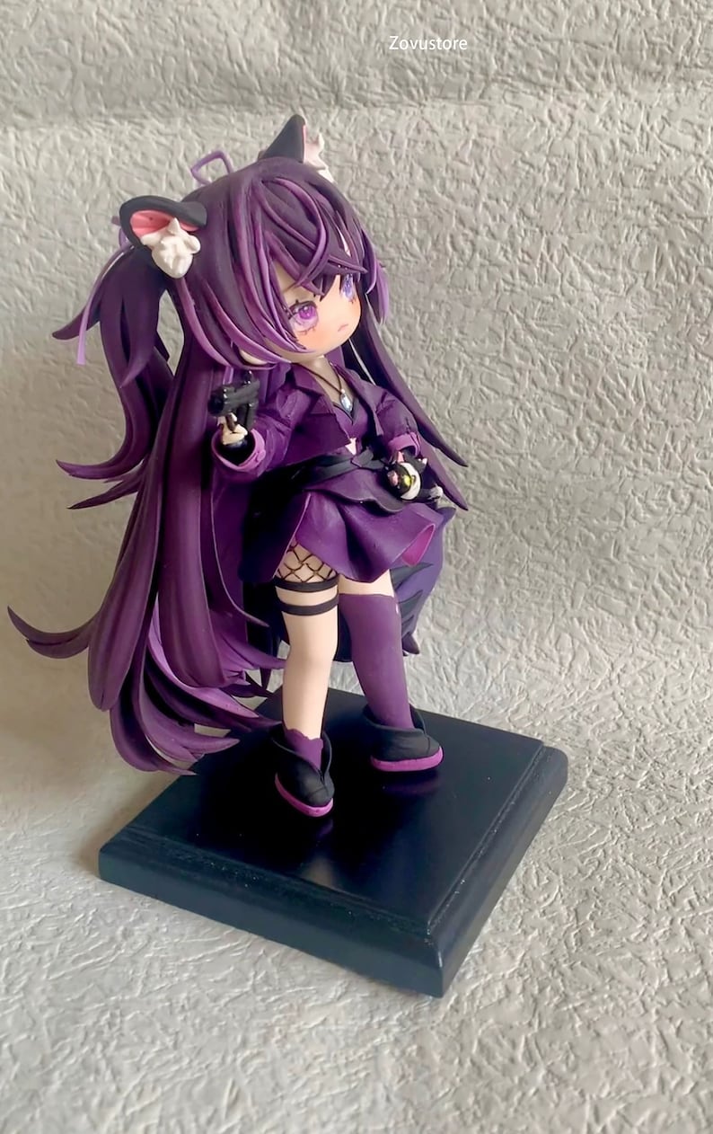 May include: Purple anime figurine with long hair, wearing a purple dress, black boots, and holding a gun. The figurine is standing on a black base.