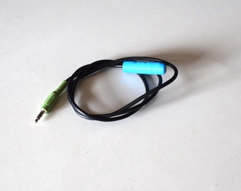May include: A black audio cable with a green and silver 3.5mm jack on one end and a light blue cylindrical component in the middle. The cable is coiled on a white surface.