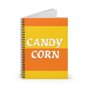 Może przedstawiać: Spiralny notatnik z okładką z motywem cukierków kukurydzianych. Okładka ma poziome paski w kolorze żółtym i pomarańczowym, z napisem "CANDY CORN" w białych, stylizowanych literach. Notatnik jest otwarty, ukazując białe strony.