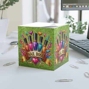 May include: A green glitter-covered notepad cube featuring a colorful nail polish design with the text "NAIL BOSS" on a banner. The design includes hearts and decorative elements, perfect for a nail technician.