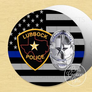 May include: A round emblem featuring the Lubbock Police badge and a Texas flag design. The badge is silver with the words "Lubbock Police Officer Texas". The flag has black and white stripes, a blue line, and white stars.