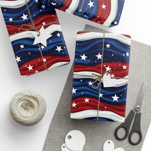 May include: Gift-wrapped presents with a patriotic design featuring red, white, and blue wavy stripes and white stars. Each package is tied with twine and a star-shaped or heart-shaped tag. A ball of twine, scissors, and blank tags are also visible.