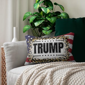 May include: Rectangular cushion featuring the word "TRUMP" in bold black letters. The design incorporates a distressed American flag, leopard print, and stars.