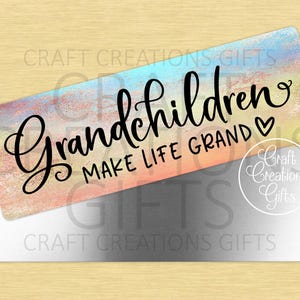 Puede incluir: Un letrero rectangular con un fondo de acuarela pastel y las palabras "Grandchildren Make Life Grand" en escritura negra. Un s&iacute;mbolo de coraz&oacute;n est&aacute; al lado de la palabra "Grand". El letrero est&aacute; sobre un rect&aacute;ngulo plateado.
